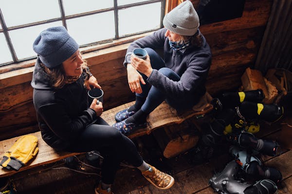 Corinne Prevot, founder of Skida enjoying a conversation in a cabin wearing Oboz Whakata Puffy slippers.