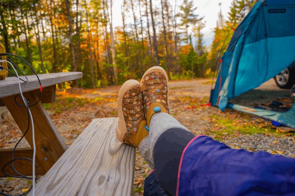 Person lodging their feet up on a campsite table wearing the Skida X Oboz Whakata Puffy during the fall time