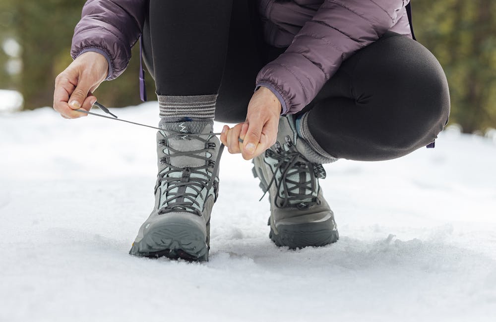 Woman lacing up the Bangtail Mid Winter insulated boot in the snow.