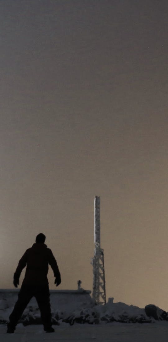 A person standing on the top of the Mt. Washington Observatory in winter at night.