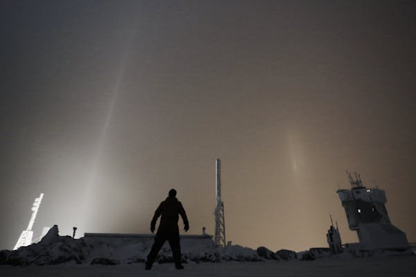 A person standing on the top of the Mt. Washington Observatory in winter at night.
