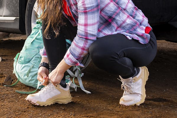 Woman tying her Katabatic Low Oboz hiking shoes before hiking on a trail.