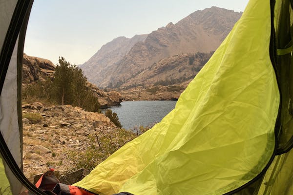 View from inside a tent looking out at a high elevation lake and mountains.