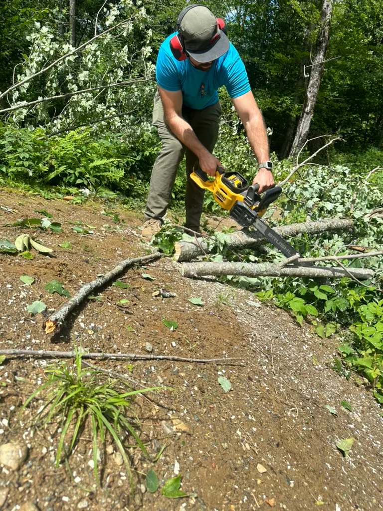 A trail builder uses a chainsaw to take downed trees off a trail.