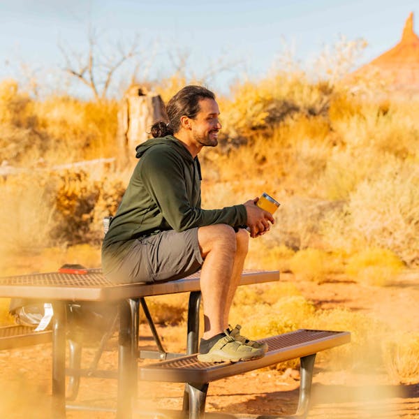 Man wearing Oboz Whakata Ease casual sandal in Conifer while drinking coffee on a bench in Moab, Utah.