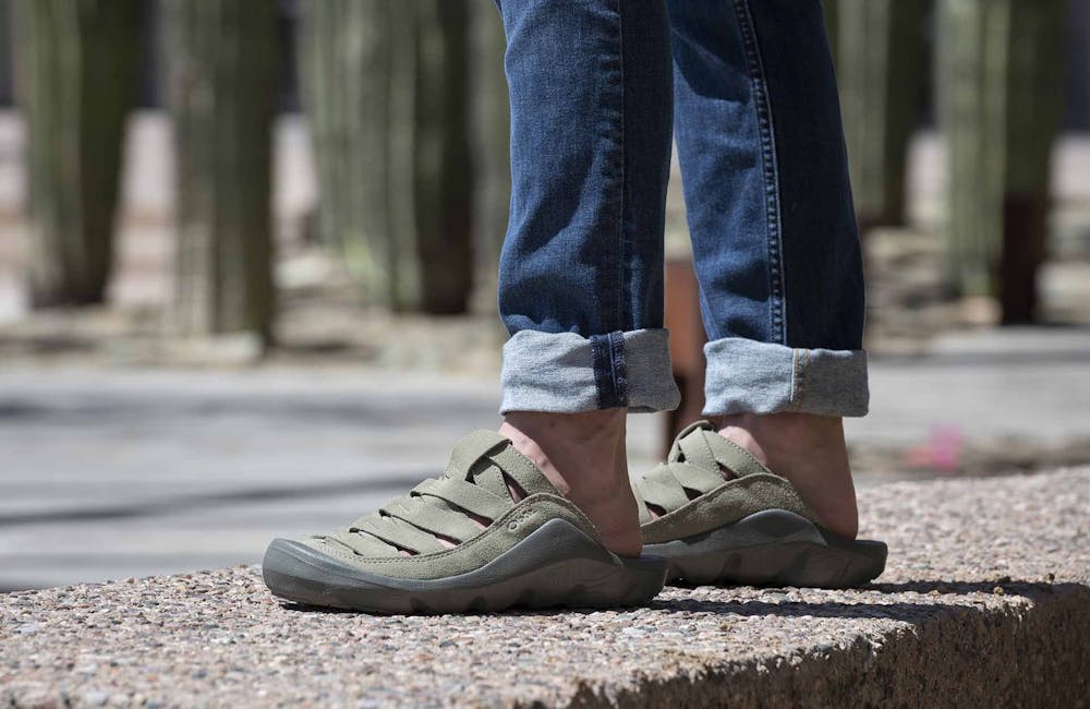 A man standing on a sidewalk wearing a pair of Oboz Whakata Town casual sandals.