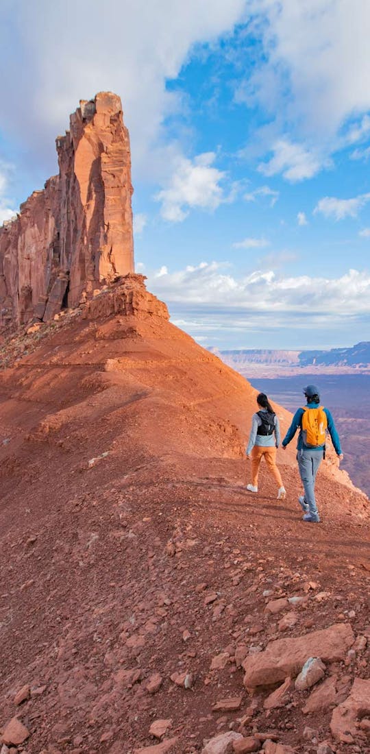 Hikers walking ridge to a giant rock formation in the Utah desert.