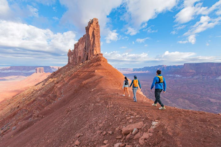 Hikers walking ridge to a giant rock formation in the Utah desert.