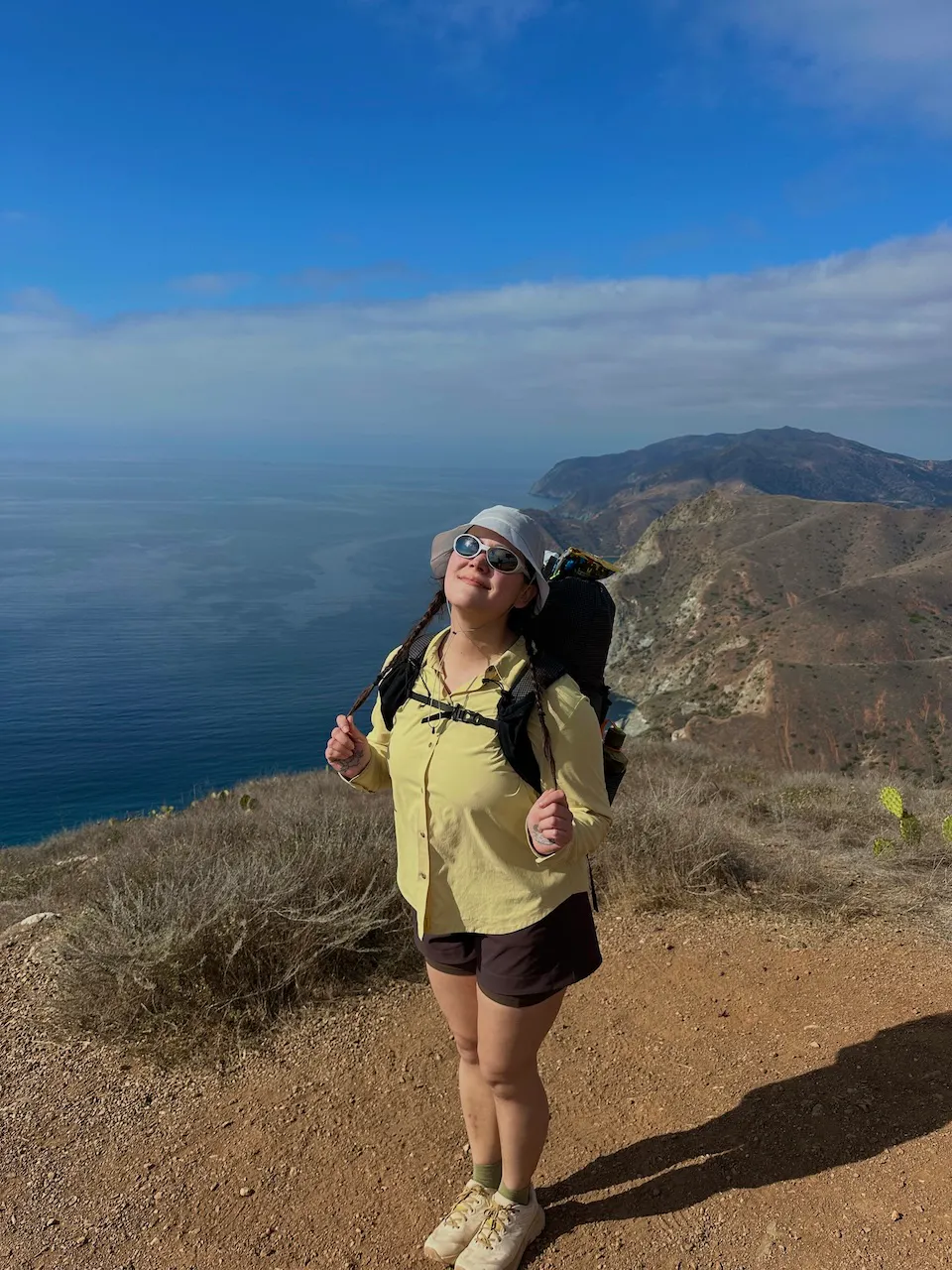 Kylie stands with a view of the coast with hiking gear