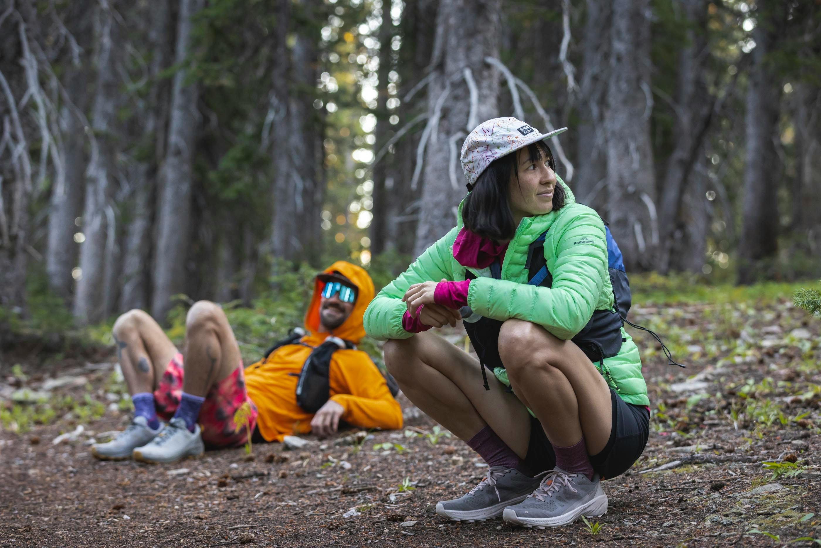 A pair of hikers rests on a trail in a dense forest wearing their Oboz hiking shoes