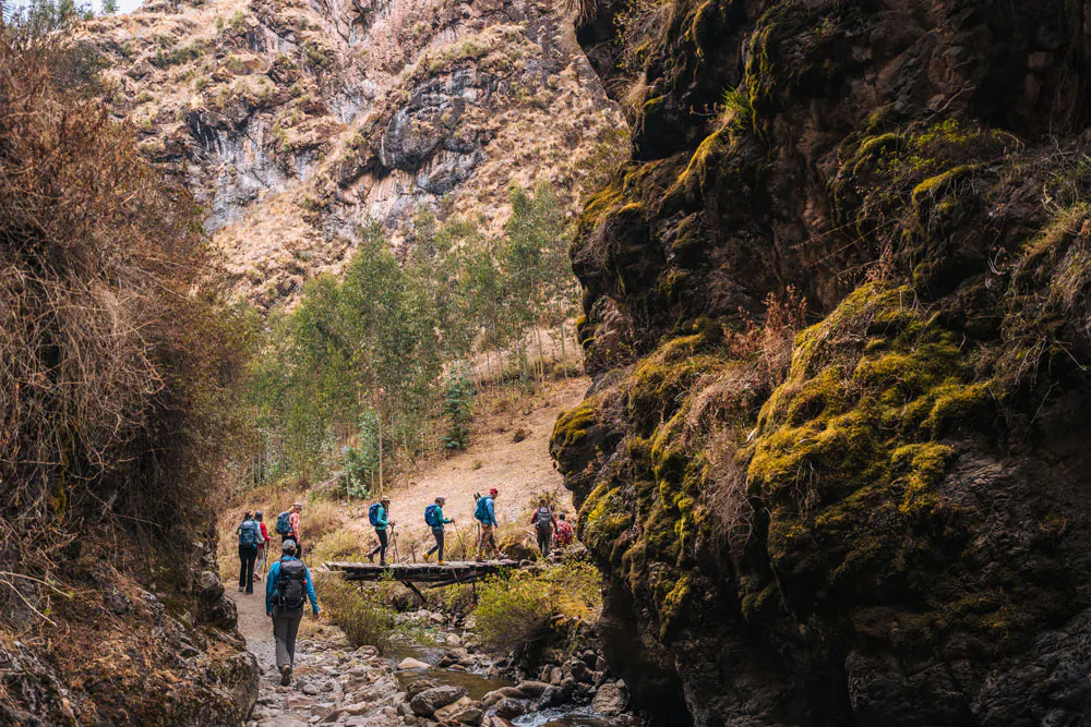 A group of hikers crosses a bridge through a canyon in Peru