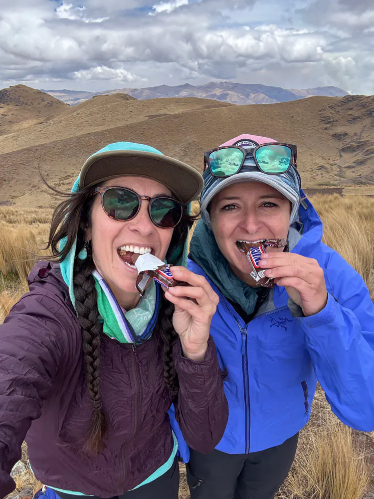 Two hikers on a backpacking trip eating a snickers.
