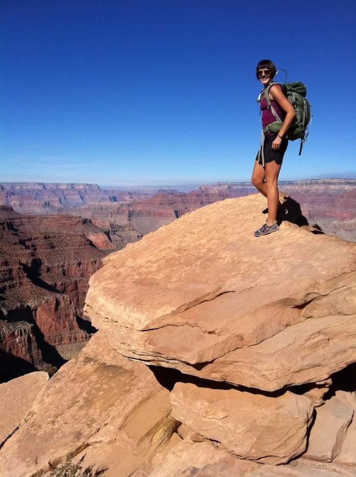 Hiker standing on top of a boulder looking over the Grand Canyon