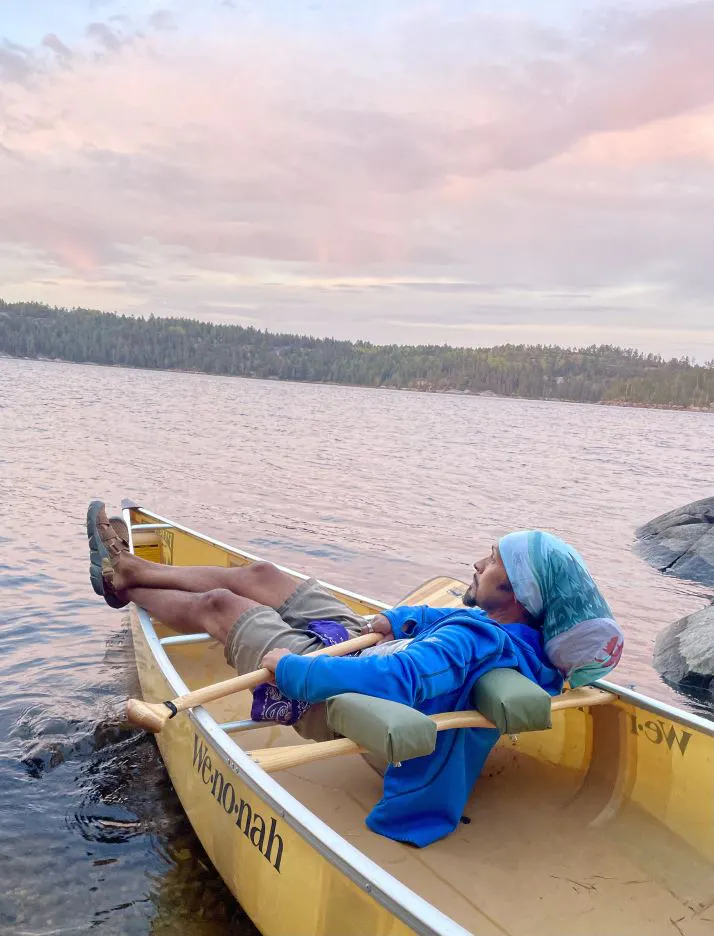 Person rests in a canoe on a lake wearing Oboz trail sandals.