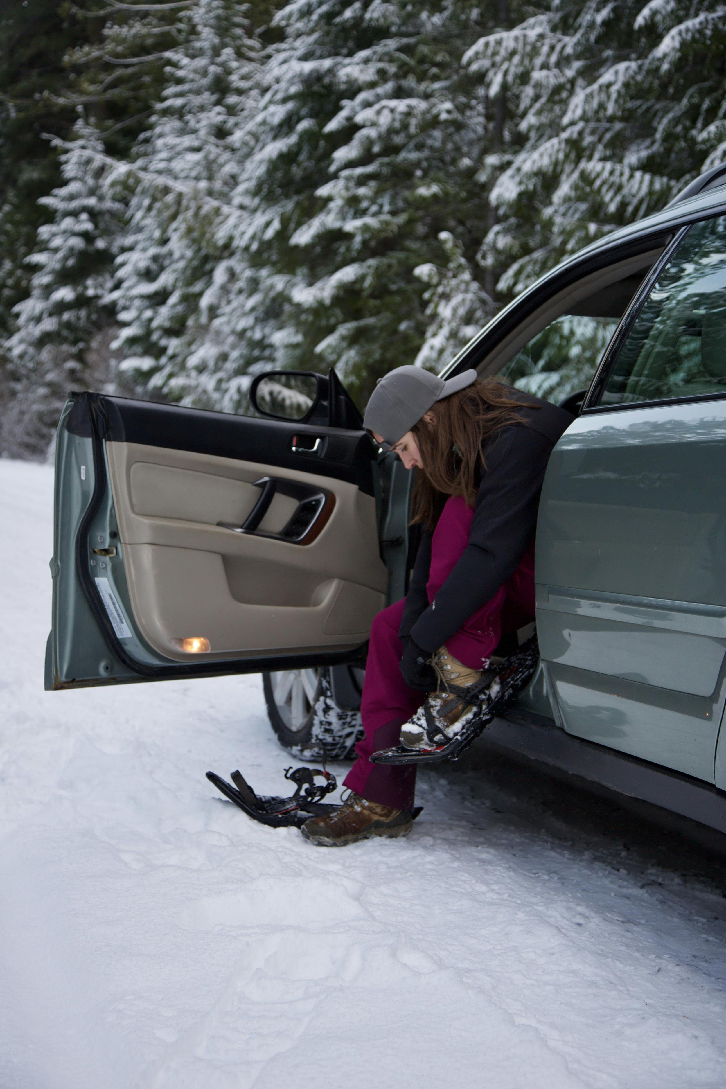 Outdoor enthusiast putting on a pair of snow shoes at the trailhead in their car.