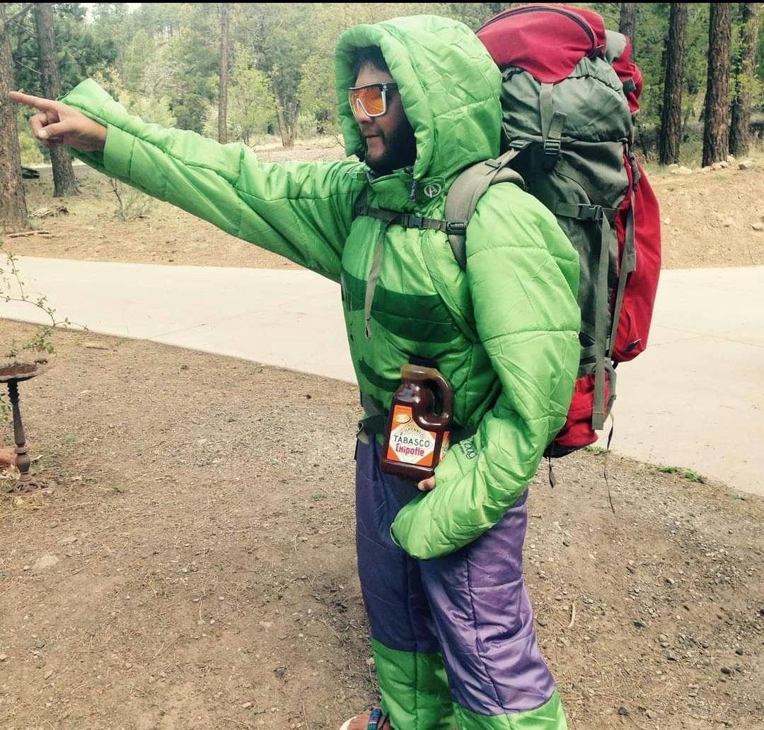 Hiker pointing down the trail wearing an insulated suit wearing a bright daypack