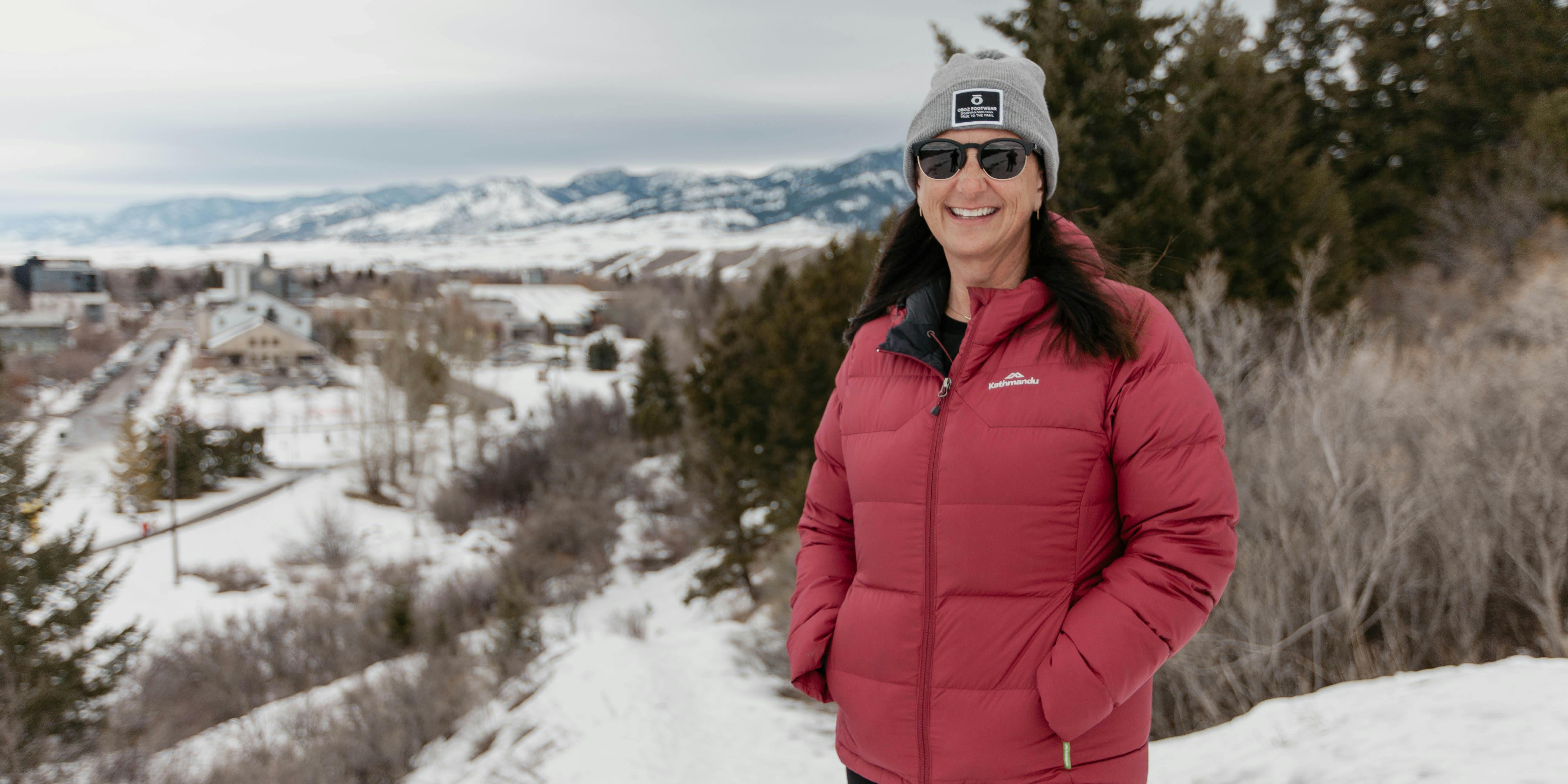 President of Oboz Footwear, Amy Beck, stands on a wintry Bozeman trail in front of downtown and the Bridger Mountain Range.