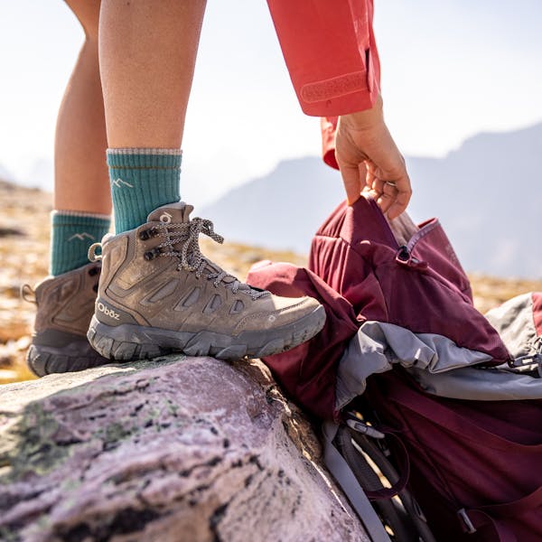 Hiker rummaging in backpack wearing the Oboz Sawtooth X Mid hiking boot.