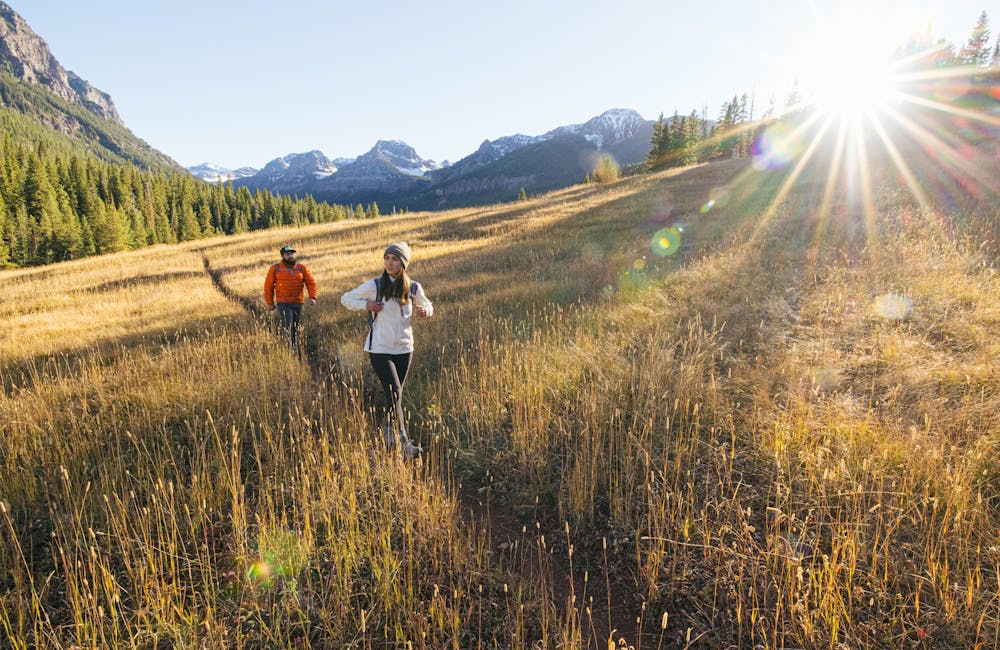 Two hikers on a trail through tall grass wearing Oboz hiking boots