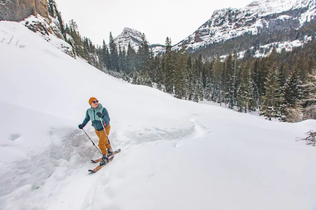A skier in the Montana back country traverses snowy terrain using approach skis to access terrain.