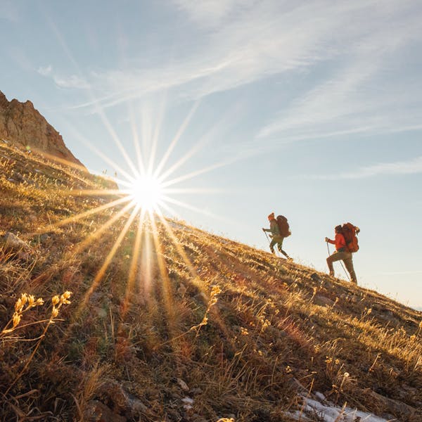 Two hikers in Oboz summiting a peak with a sun flare.