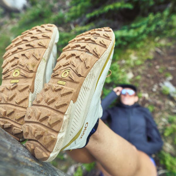 Woman stretching on a tree showing off her Oboz Katabatic wind trail running shoes.