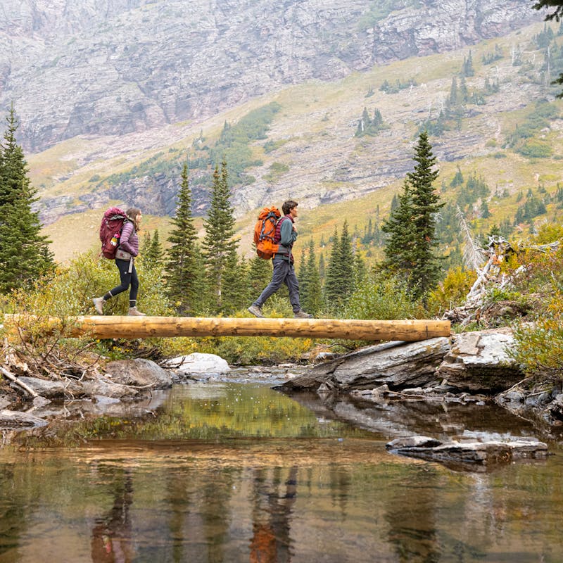 Hikers backpacking across a log bridge in the Oboz Sawtooth X hiking boots