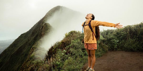 Woman on top of a mountain peak in Hawaii after climbing a muddy mountainous trail.