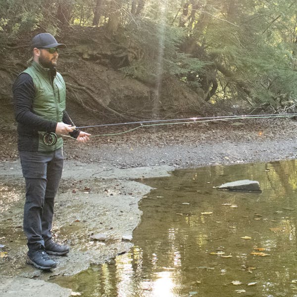 Man fly fishing on a creek bank in the Oboz Arete Mid hiking boots.