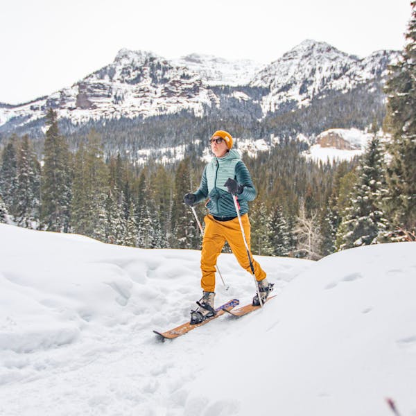 Woman backcountry skiing in on a snowy mountainous trail while wearing Oboz winter boots.