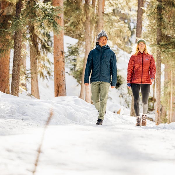A couple waking on a snowy trail in the woods wearing Oboz insulated boots.