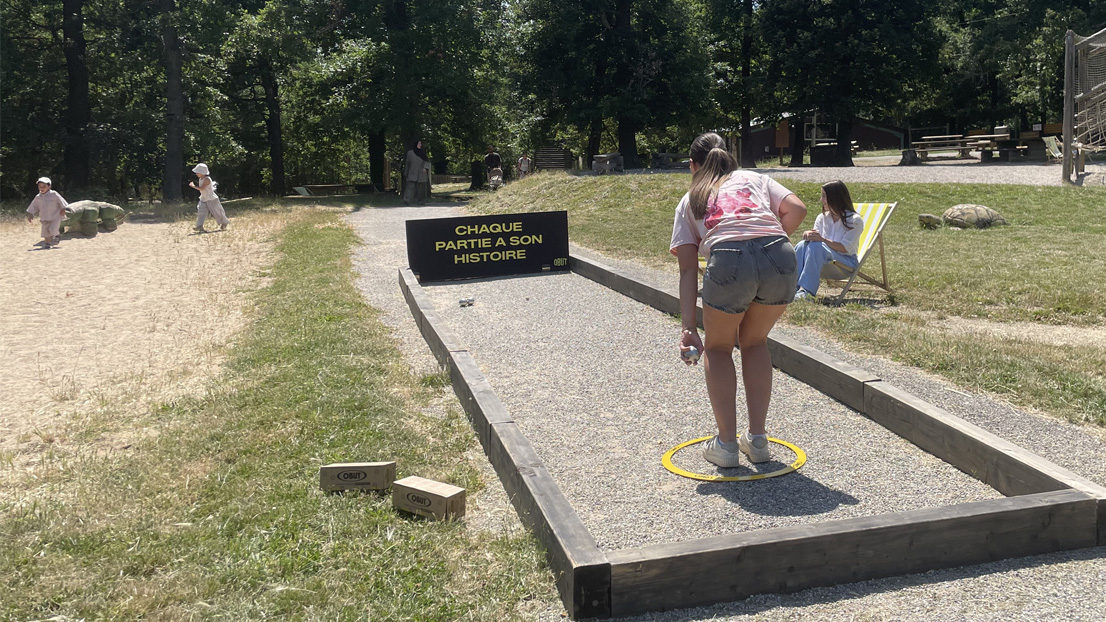 Una niña lanzando una bola de petanca en una pista de petanca en Peaugres.