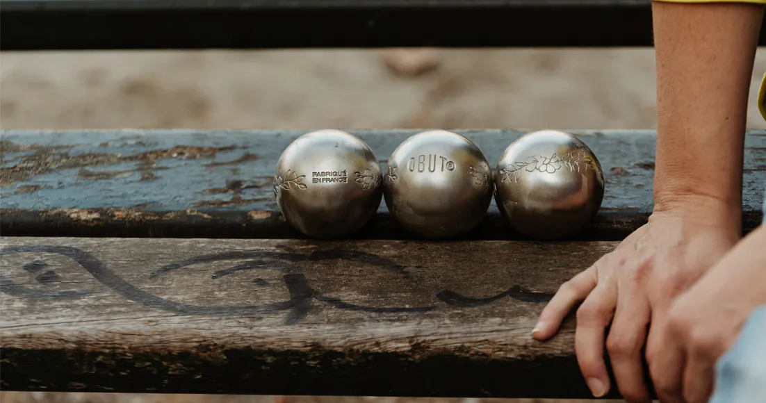 Trois boules de pétanque posées sur un banc avec une personne assise