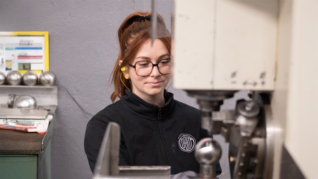 Amaurie, agente de production Obut devant sa machine avec une boule de pétanque