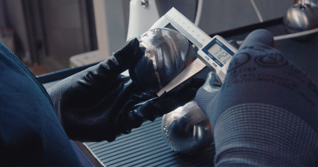 Contrôle avec précision du diamètre d'une boule de pétanque par une agente de production