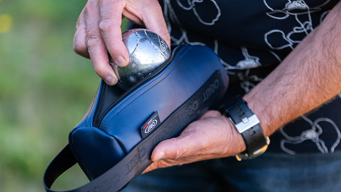 Hand legt eine Obut Pétanque-Kugel in eine Tasche