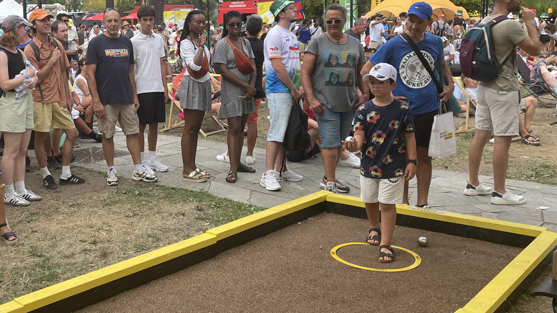 Un enfant jouant à la pétanque avec des gens autour lors d'un événement