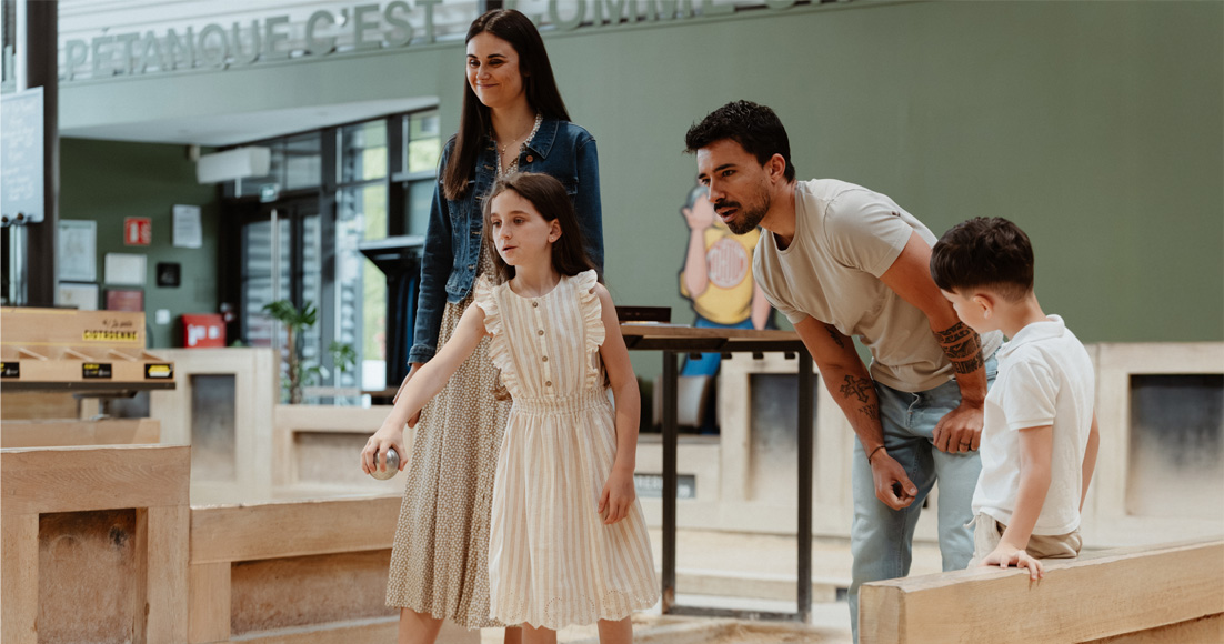 Un couple et ses deux enfants jouant à la pétanque. La petite fille lance la boule de pétanque