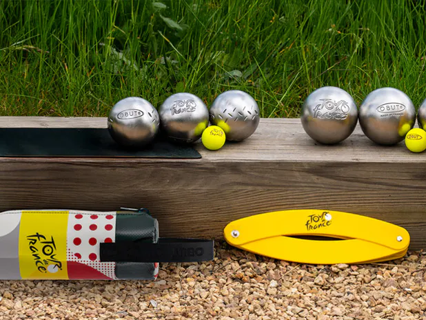 Boules de pétanque et accessoires au logo du Tour de France posés au bord d'un terrain de pétanque