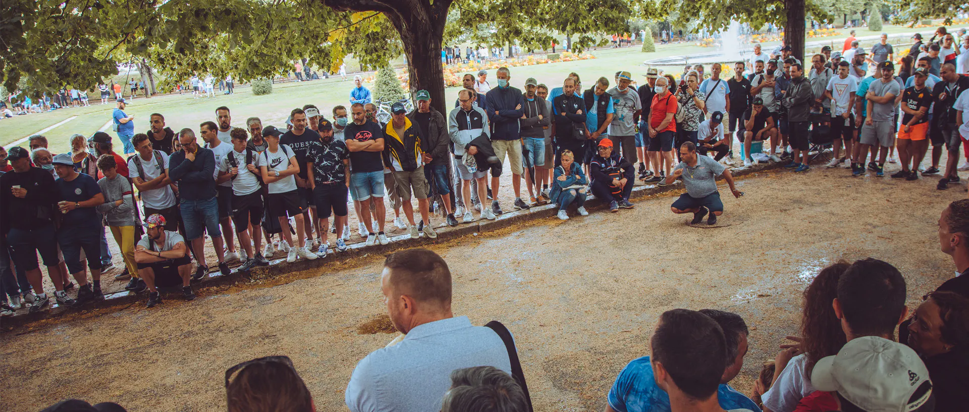 Ein Pétanque-Spieler wirft seine Kugel auf einem Spielfeld, umgeben von Zuschauern