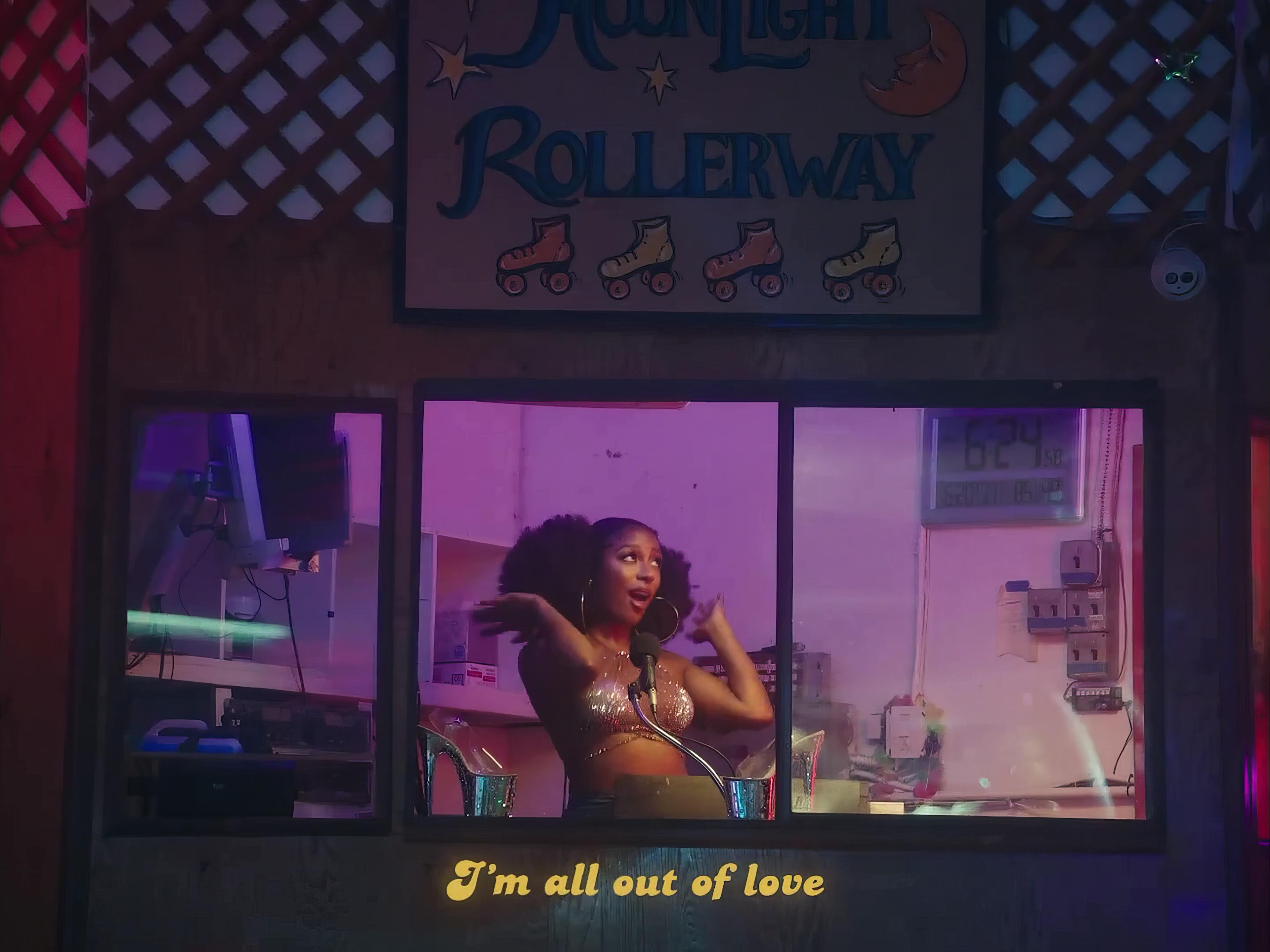 A woman in a sparkling outfit performs in a roller rink DJ booth with neon lights and a 'Moonlight Rollerway' sign above, evoking a lively, retro atmosphere.