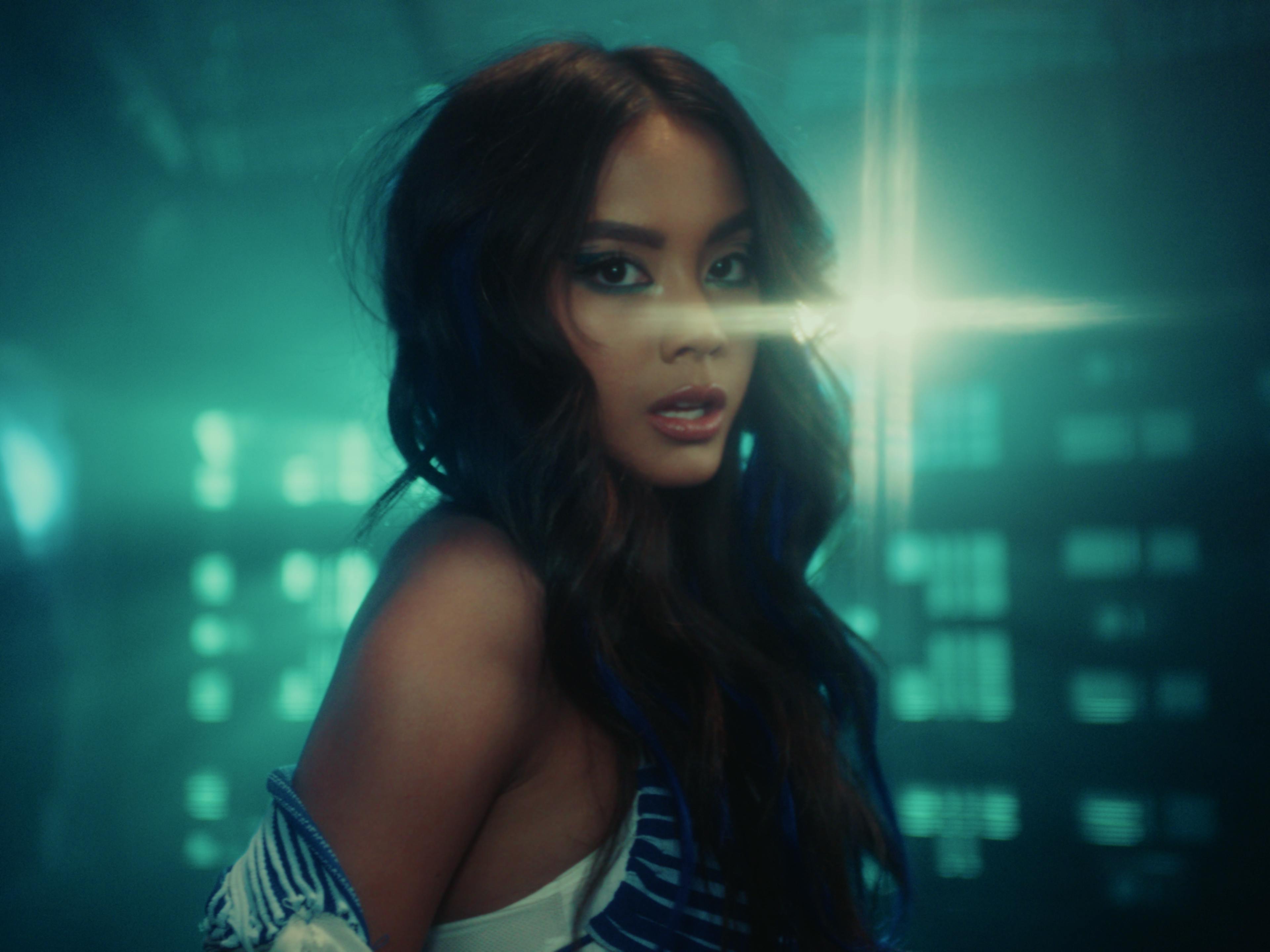 A medium shot of Ylona Garcia as she looks at the camera, dancing inside of a moody teal spaceship