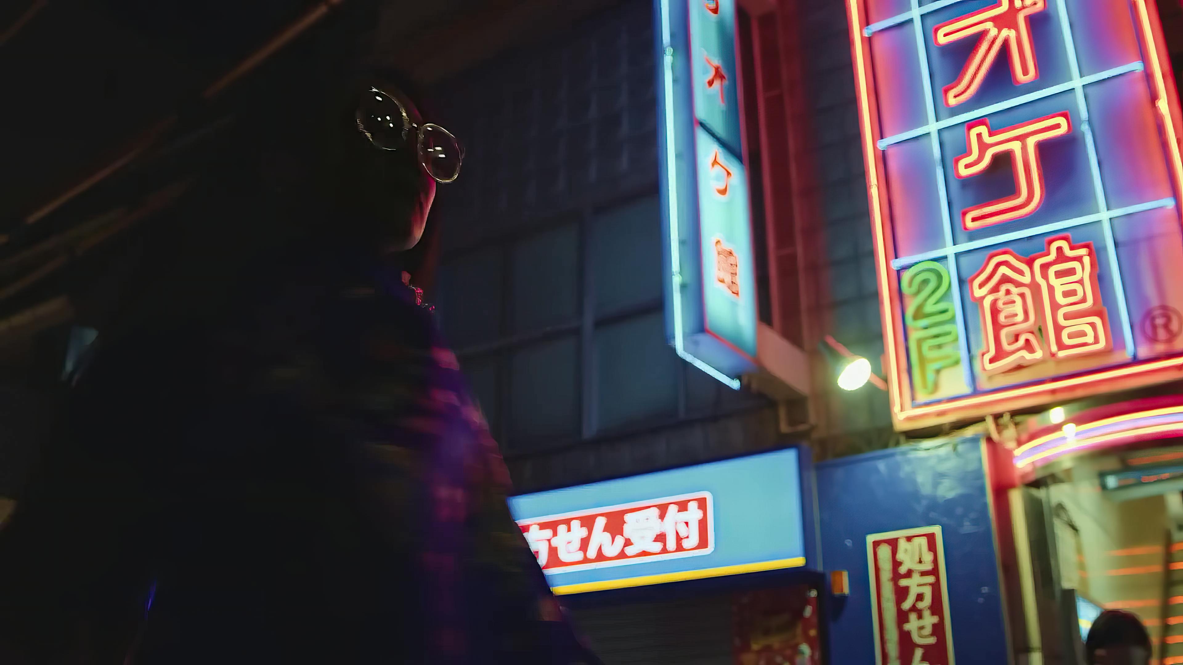 A silhouette of a person wearing round glasses facing neon-lit signage in a bustling urban night scene, evoking a sense of anticipation and the urban nightlife.