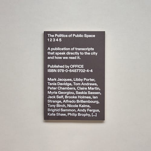 A photo of a black book cover with white text reading "The Politics of Public Space 1 2 3 4 5: A publication of transcripts that speak directly to the city and how we read it."