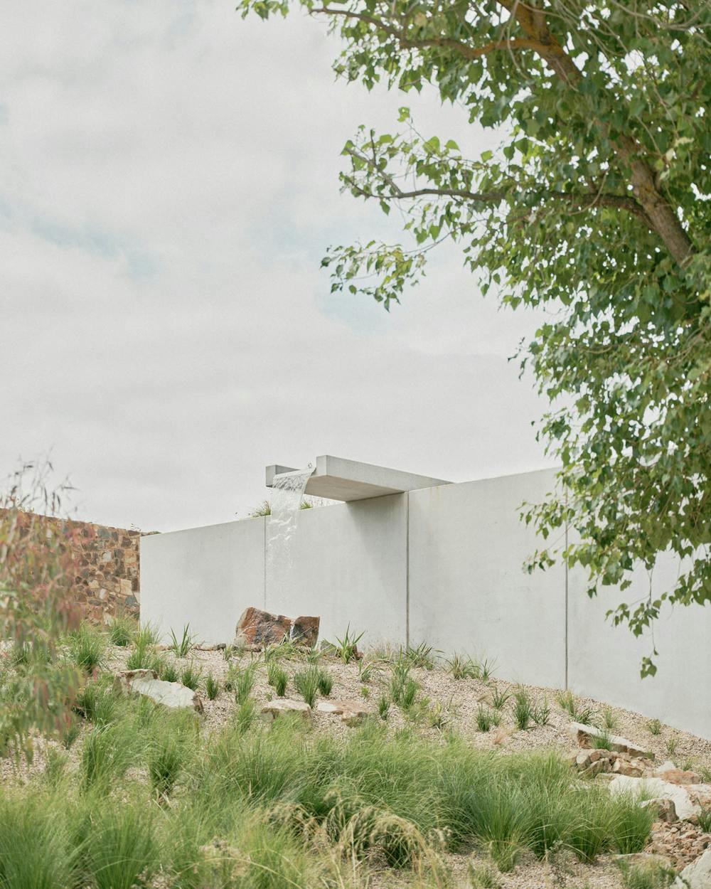 A photograph of a falling water feature. Waterflows onto a rock, set in a landscape filled with grasses. 