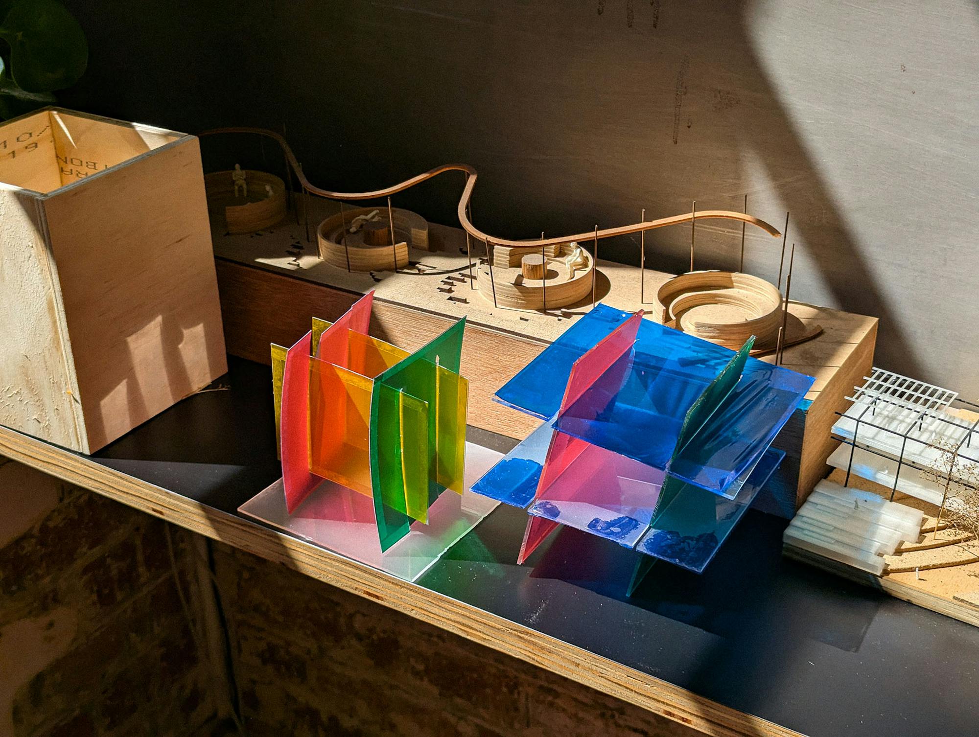 A photo of abstract, brightly coloured, translucent, architectural model, surrounded by timber models.