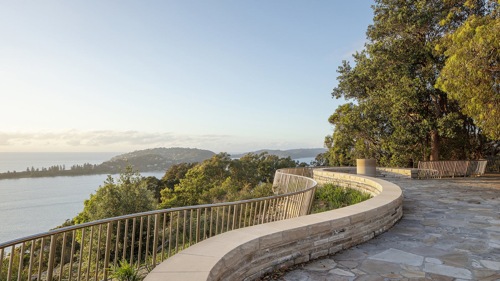 A photograph of Sydney lookout with a curved sandstone wall and lower metal balustrade. There are trees above and below.