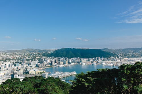 Photograph of a view over a developed waterfront city from a mountain, another mountain is in the city, with more in the distance.