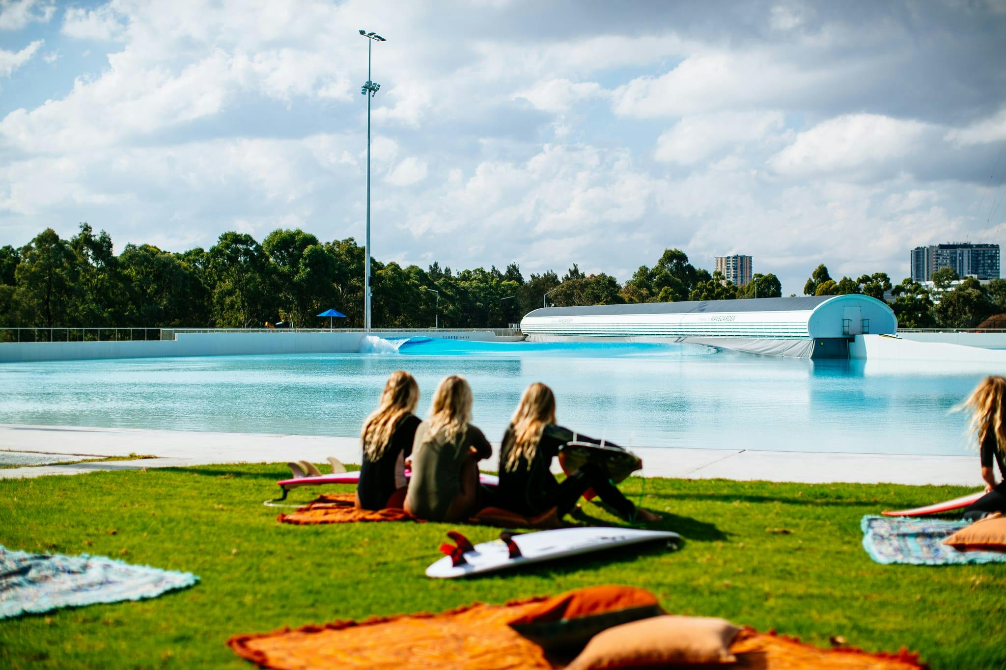 A photograph of people sitting on the grass beside a large wave pool. 