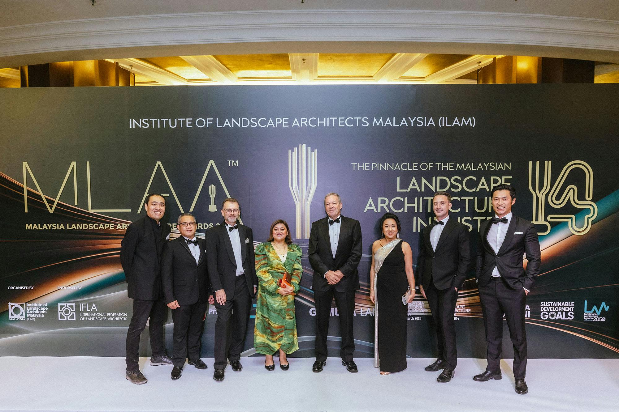 A photo of eight smiling people in formal attire, standing on a 'white carpet'